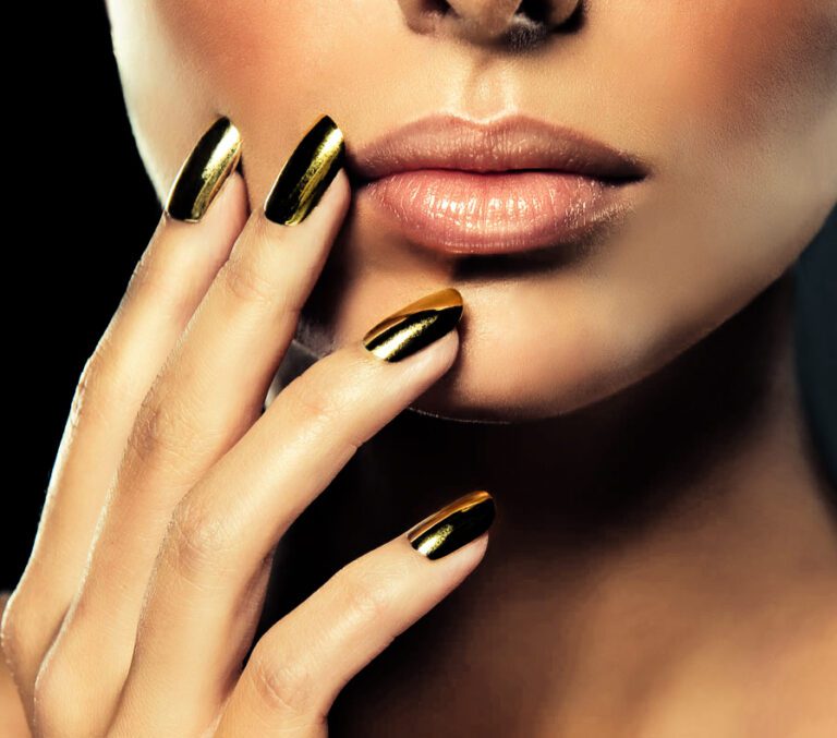 Eine Frau mit goldenen Neumodellage-Nägeln und schwarzem Hintergrund.