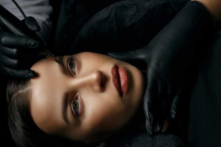 Eine Frau lässt sich in einem dunklen Raum die Augenbrauen wachsen und neu modellieren.
