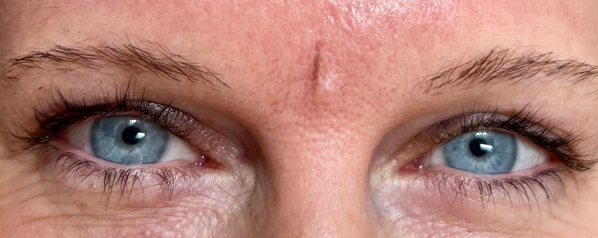 Eine Nahaufnahme der Augen einer Frau mit Microblading auf den Augenbrauen und blauen Augen.