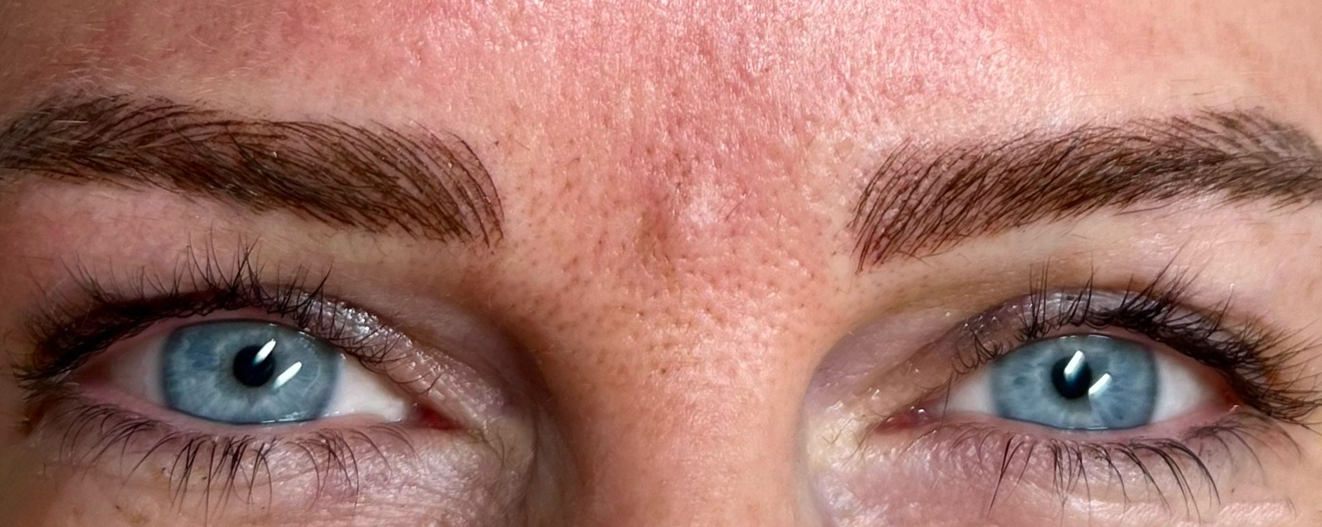 Eine Nahaufnahme der Augen einer Frau mit blauen Augen und Microblading.